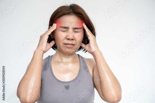Sweaty Asian woman in grey sportswear touching temples, suffering from an intense headache, migraine, heat stroke, or dehydration after a sport workout session at home