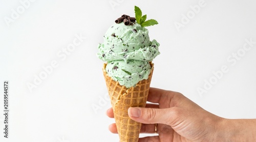 Mint chocolate chip ice cream cone in hand with fresh mint leaves in bright studio lighting on white background for summer dessert advertising.