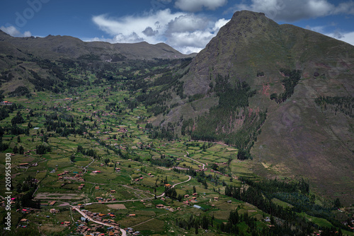 Fotografie Patchwork farms and trees fill a green Andean valley beneath a steep rounded mountain and cloud shadows in the Sacred Valley