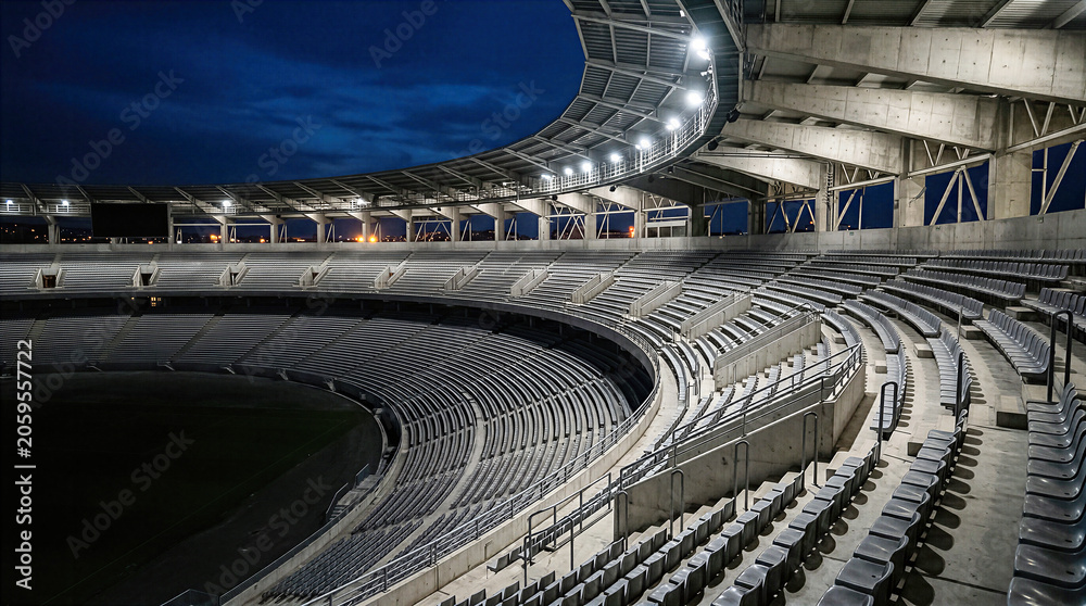 Obraz premium Empty professional stadium seating showing curved grey concrete grandstands illuminated under night lights presenting abstract minimalist modern architectural patterns displaying impressive vast space