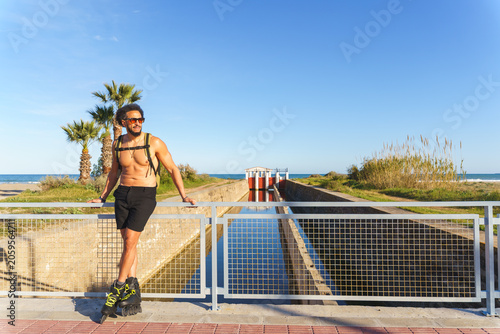 Foto Shirtless latino man with rollerblades enjoying outdoor activity by a beach cana