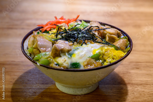 Delicious Oyakodon, Japanese chicken and egg rice bowl topped with shredded nori seaweed and red pickled ginger, served in a ceramic bowl on a wooden table. Comfort food concept.