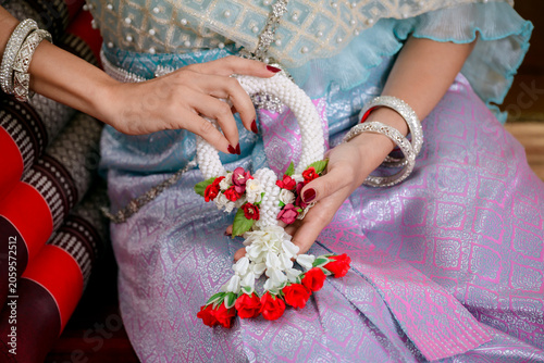 Close up of a woman in elegant traditional Thai dress holding a beautiful handmade flower garland (Phra Malai) with silver ornaments. Cultural heritage and wedding concept.