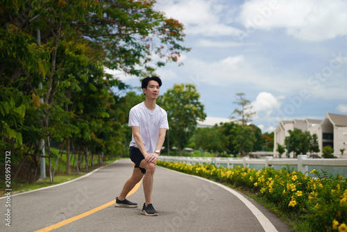 Young Asian Man Stretching on Scenic Park Path Before Running Workout Outdoors