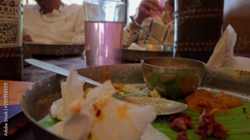 Leftovers rest on a banana leaf Sadhya thali next to pink Pathimugam water. In the background, diners hold glasses, enjoying the traditional Kerala Ayurvedic drink after finishing their authentic meal