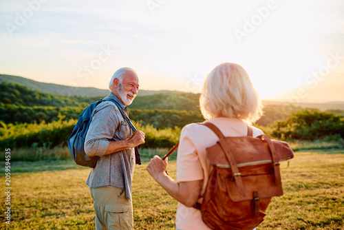 Tableau sur toile Happy senior couple hiking on a grassy hill, carrying backpacks, and enjoying a
