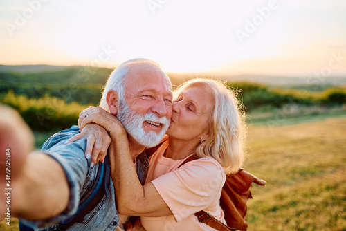 Happy senior couple embracing and taking a selfie outdoors during sunset  enjoying love and retirement in nature