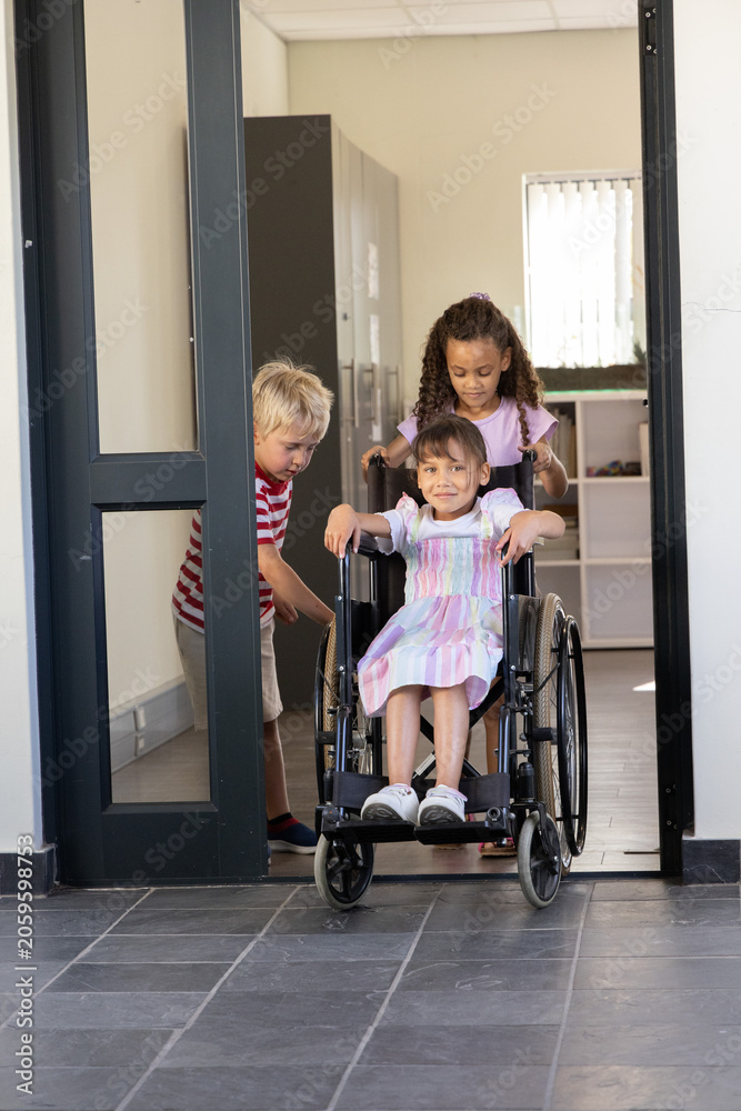 Obraz premium Three school-age children pushing manual wheelchair through doorway at classroom with tiled floor