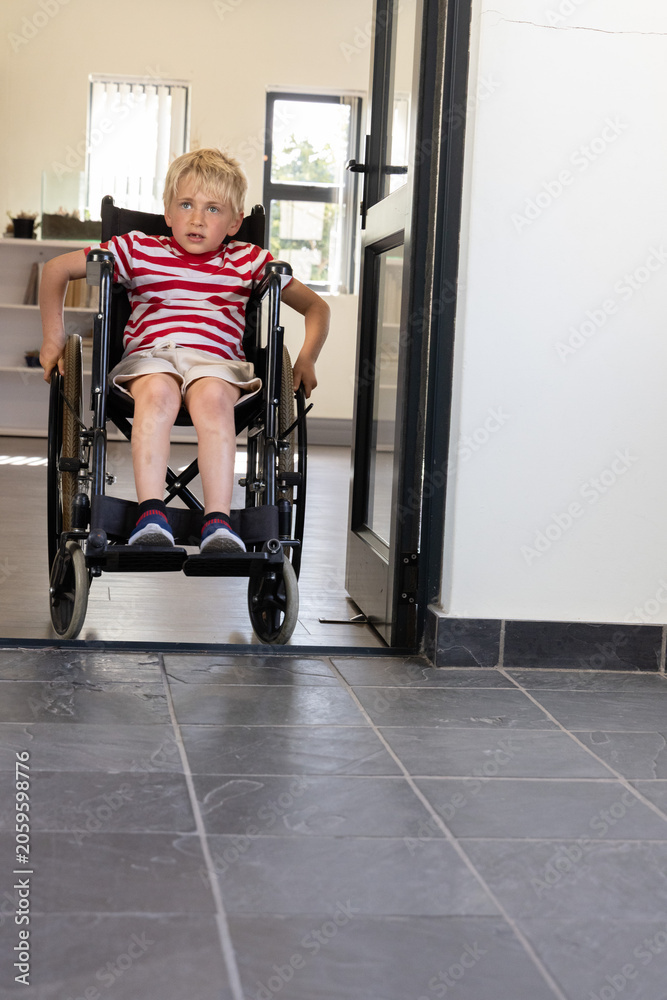 Obraz premium Boy aged six to eight pushing wheelchair with hand rims through home doorway, wearing striped shirt