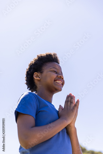 African American male child standing smiling while pressing hands at chest wearing blue tee at park