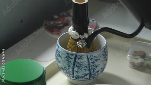 4K pouring hot water from kettle into clear glass bowl with vibrant green matcha powder on white table, Traditional Japanese tea preparation and healthy drink concept.