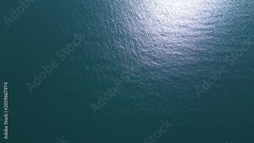 Aerial top down view of a blue sea water surface with sun reflection