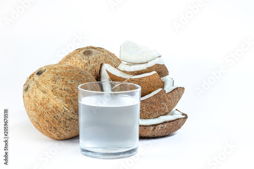 Fresh coconut water in a clear glass with whole and sliced coconuts on white background, minimal style, refreshing and healthy concept