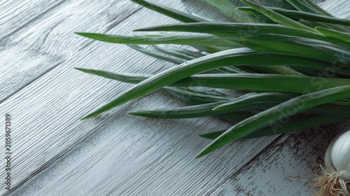 Fresh green shoots of an allium vegetable rest upon weathered light colored wooden planks with a bulb visible nearby.