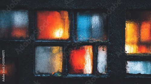 Illuminated interior spaces cast warm, contrasting colors through a grimy, textured exterior windowpane.