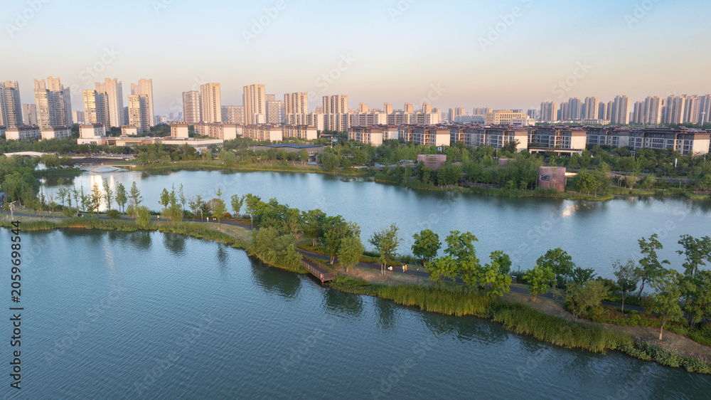 Fototapeta premium Aerial View of Urban Lake Park and Modern City Skyline at Sunset