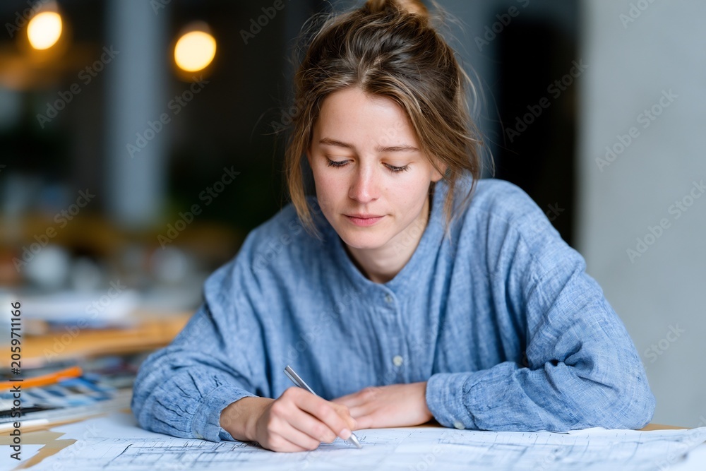 Obraz premium Focused young woman working on architectural plans in a bright office environment