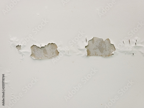 A damaged white wall showing severe peeling paint and bubbling from moisture or water leakage revealing raw plaster.
