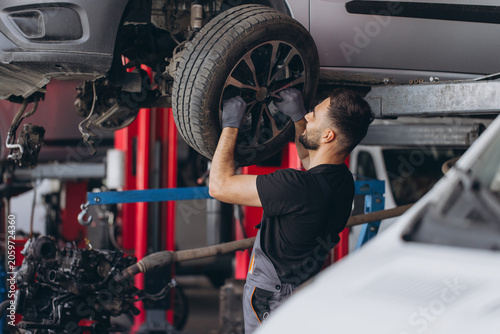 Quadro su tela Auto mechanic changing a tire on a raised car in a garage, performing wheel serv