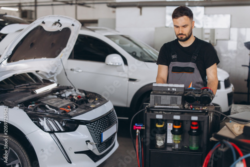 Canvastavla Car mechanic diagnosing vehicle with open hood in auto repair shop, performing m