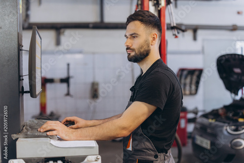Auto technician performing digital car diagnostics on a monitor, checking vehicle systems in a modern professional workshop