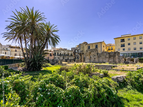 The historic Greek Temple of Apollo surrounded by green gardens and palms in Pancali Square, Ortigia. Travel photography of famous ancient monument ruins in Syracuse, Sicily.