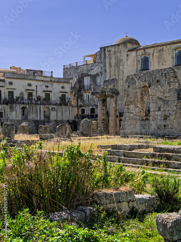 Vertical image of the Temple of Apollo with the San Paolo Apostolo church background in Ortigia, Syracuse, Italy. Historic archaeological site and old town buildings in Sicily.