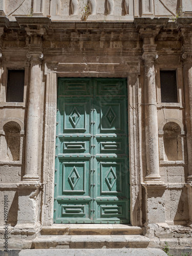 Traditional massive green entry portal featuring elegant geometric diamond carvings in Siracusa, Italy. Scenic front exterior of an old town historic church or mansion.