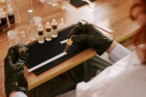 High angle shot of woman testing essential oil, filling dropper bottle and testing sample in lab setting. Suitable for skincare production, beauty brand marketing and perfume production
