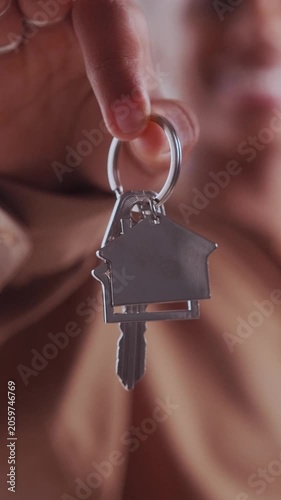 A happy young African American homeowner holds up a brand new shiny key ring with a house shaped key holder, proud of buying her first real estate property and achieving homeownership.