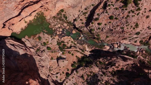 Drone footage twisting straight down into El Chorro's canyon floor, exposing emerald rock pools, white water, a narrow cliff path, and sun-scorched boulders in vivid detail.