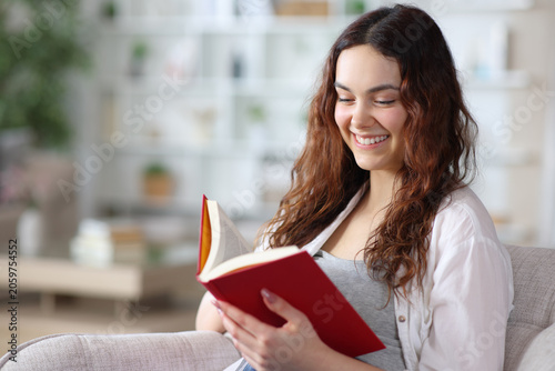 Happy young woman reading a red paper book on a chair