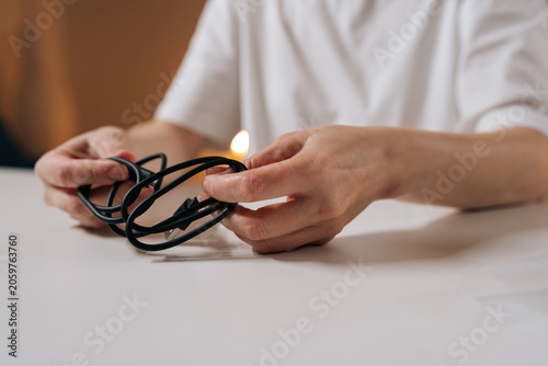 Valokuva Close-up cropped shot of unrecognizable person hands untangling knotted black power cord sitting at white table, preparing charging cable for use and restoring order to tangled wire