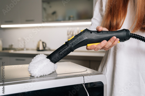 Φωτογραφία Cropped shot of housewife cleaning microwave top with steam cleaner, removing grease and germs for spotless kitchen appliance