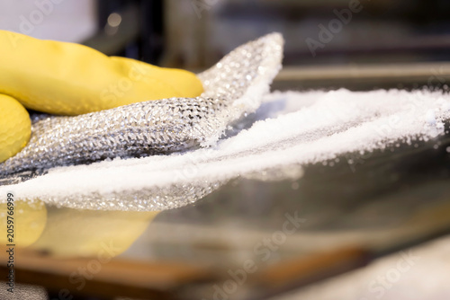 Person cleaning oven door glass using bicorbonate soda and a scouring pad. Household cleaning chore concept.