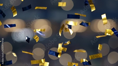 Golden and blue confetti falling against a bokeh background, celebrating a festive occasion.