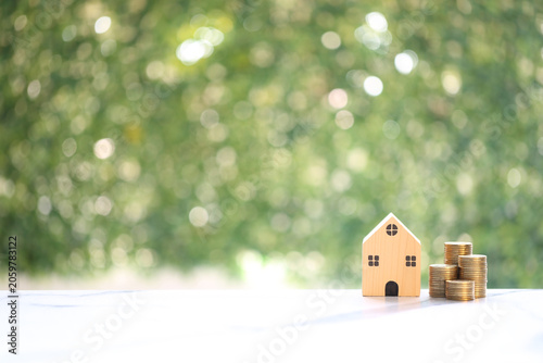 Miniature wooden house model beside five stacks of gold coins arranged in ascending order, representing the concept of financial growth, saving money for a house and investment success.