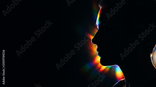 Ethereal profile silhouette of a human head, dramatically backlit by a radiant spectrum of rainbow light, evoking mystery and introspection against a deep dark backdrop