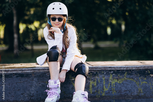 Photos Teenage girl wearing helmet, sunglasses, knee pads, and roller skates, sitting o