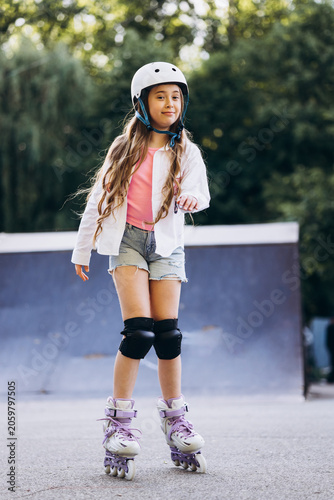 Young child wearing helmet and knee pads, confidently moving on rollerblades in a skate park during summer