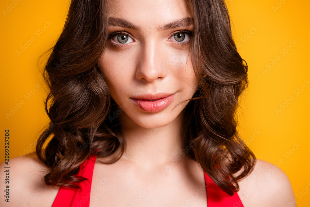 Fototapeta premium Young woman portrait with wavy brown hair and soft makeup wearing a red top against a vibrant yellow background, confident beauty close-up