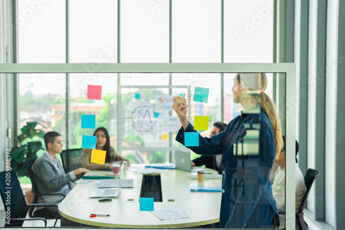 Professional manager maps concepts on glass wall during collaborative workshop. Team members contribute insights and support creative problem solving for business growth.