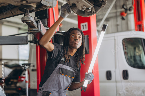 Young african american auto mechanic fixing car with tool and examining brake system in workshop garage