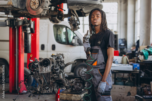 Foto Young African American auto mechanic holding an impact wrench, working in a prof