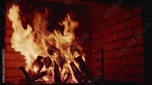 A cozy burning bonfire with bright orange flames and glowing logs inside a brick fireplace or barbecue area.