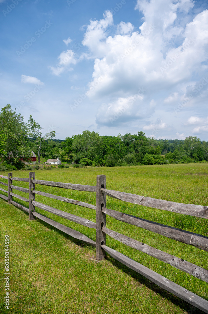 Obraz premium Split rail wooden fence aiong idyllic green pasture under blue sky treelined background ranch horse farm