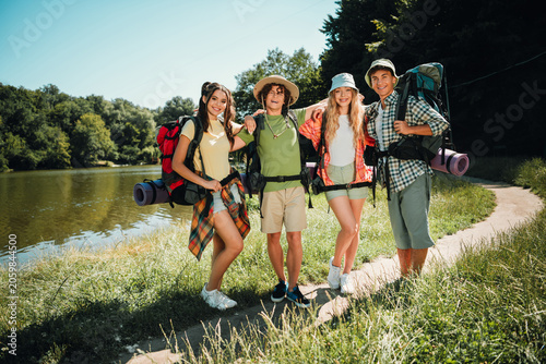 Φωτογραφία Four teenage friends hiking together by a lakeside trail with backpacks and camp