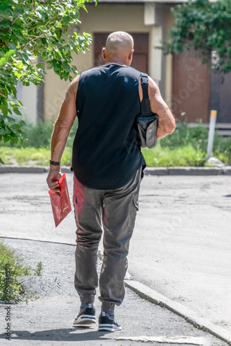 A man with a shoulder bag walks along the sidewalk on a summer day