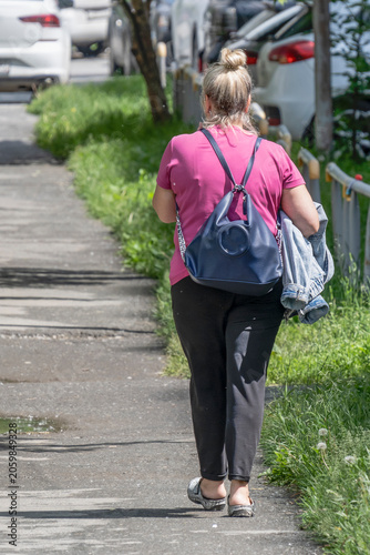 A woman with a backpack walks along the sidewalk on a summer day