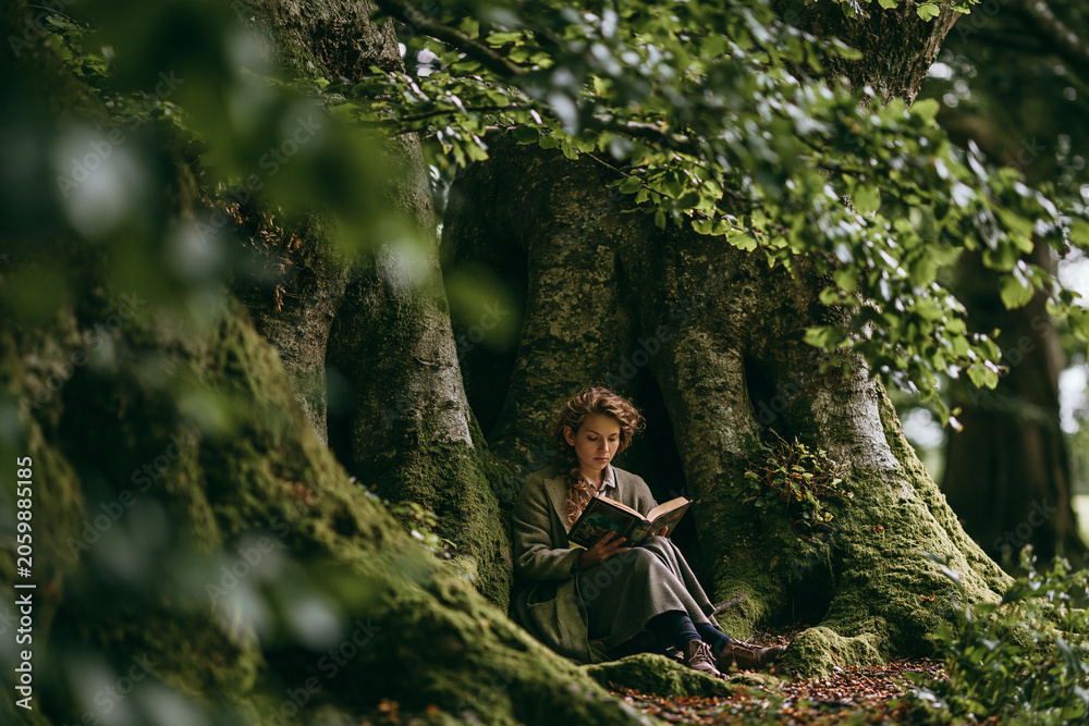 Fototapeta premium Reader immersed in the magic of a story beneath ancient trees in nature
